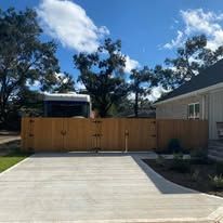 Wooden fence and gate with concrete driveway, blue sky.