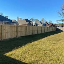 Wooden fence along a grassy yard, houses in the background on a sunny day.