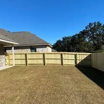 A backyard with a wooden fence and a house under a clear blue sky.