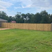 Wooden fence surrounding a grassy backyard on a cloudy day.