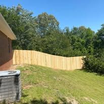 Wooden fence in a grassy yard, trees in the background, blue sky.