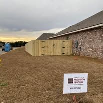 Wooden fence bordering a brick building; sign in foreground advertises fencing services.