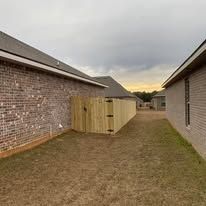 Backyard with brick house, wooden fence, and grass. Cloudy sky in background.