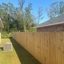 Wooden fence in a backyard, with an air conditioning unit and a house visible in the background on a sunny day.