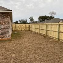Brick house next to a wooden fence enclosing a grassy backyard.