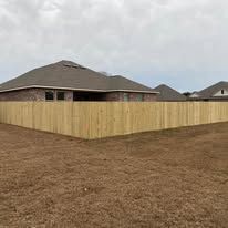 Wooden fence surrounds a house with a brown roof on a cloudy day.