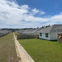 Row of houses with green lawns and a concrete drainage ditch under a cloudy sky.