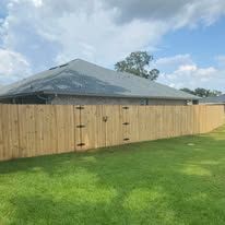 Wooden fence surrounding a house with a green lawn under a cloudy sky.