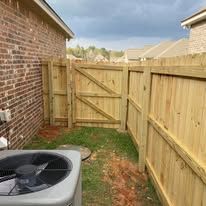 Exterior view of brick building, wooden fence and gate. Air conditioning unit in foreground.
