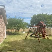 Wooden playground in a grassy backyard next to a brick building.
