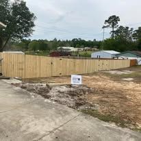 Wooden fence surrounding a property on a cloudy day. A sign is placed in front of the fence.