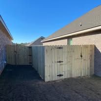 Wooden fence surrounding a backyard, with a brick house on the left and a building in the background under a blue sky.