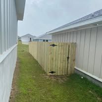 Wooden fence with black hardware separating yards; adjacent to a house with white siding.