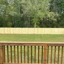 Wooden deck railing overlooking a grassy yard and a wooden fence. Trees are in the background.