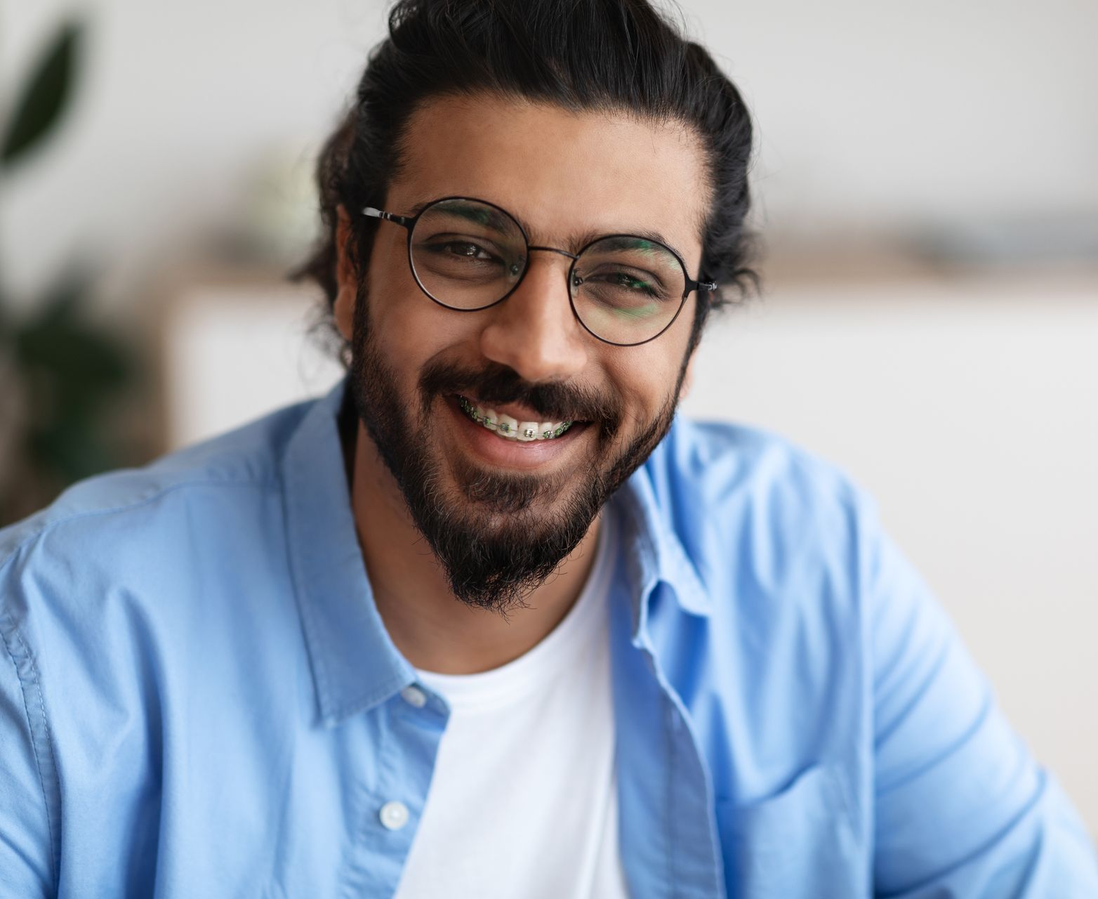 Man with beard, glasses, and braces smiles widely, wearing a blue shirt.