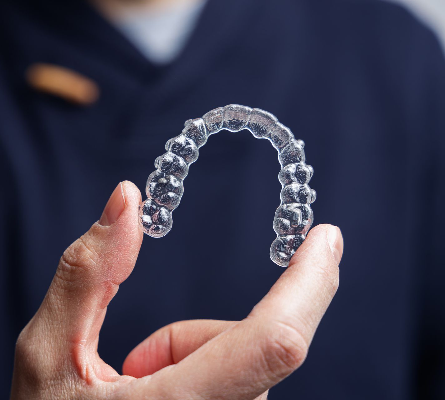 Person holding a clear, plastic dental aligner, likely for teeth straightening.