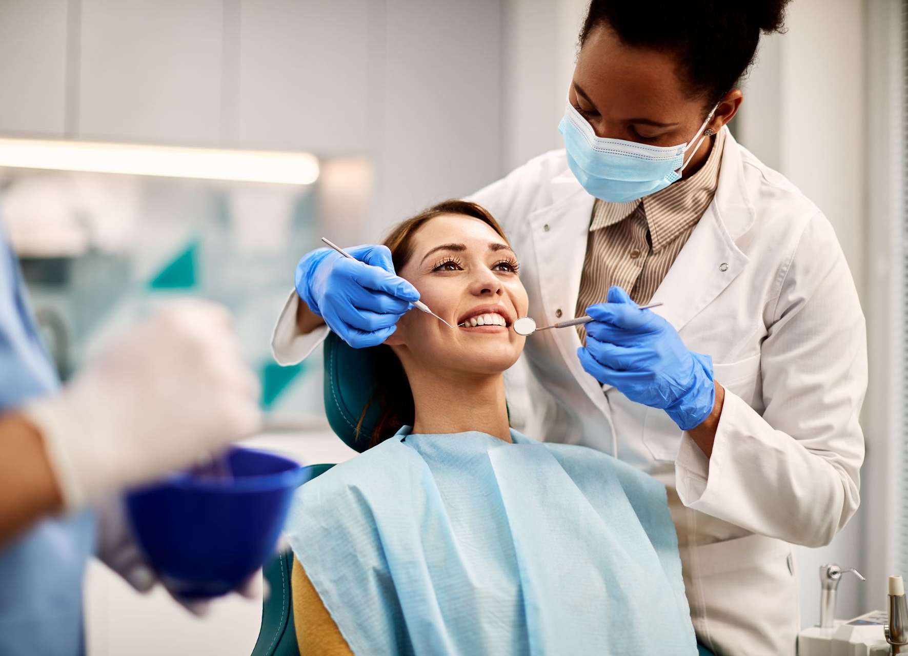 Dentist examines a smiling patient's teeth in a dental office; doctor wears mask and gloves.