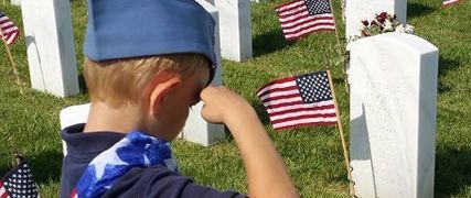 A young boy is saluting a grave in a cemetery.