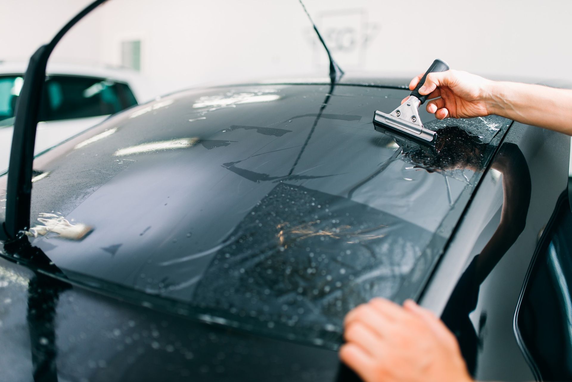 Person applying tinted film to a car's rear window, using a squeegee.