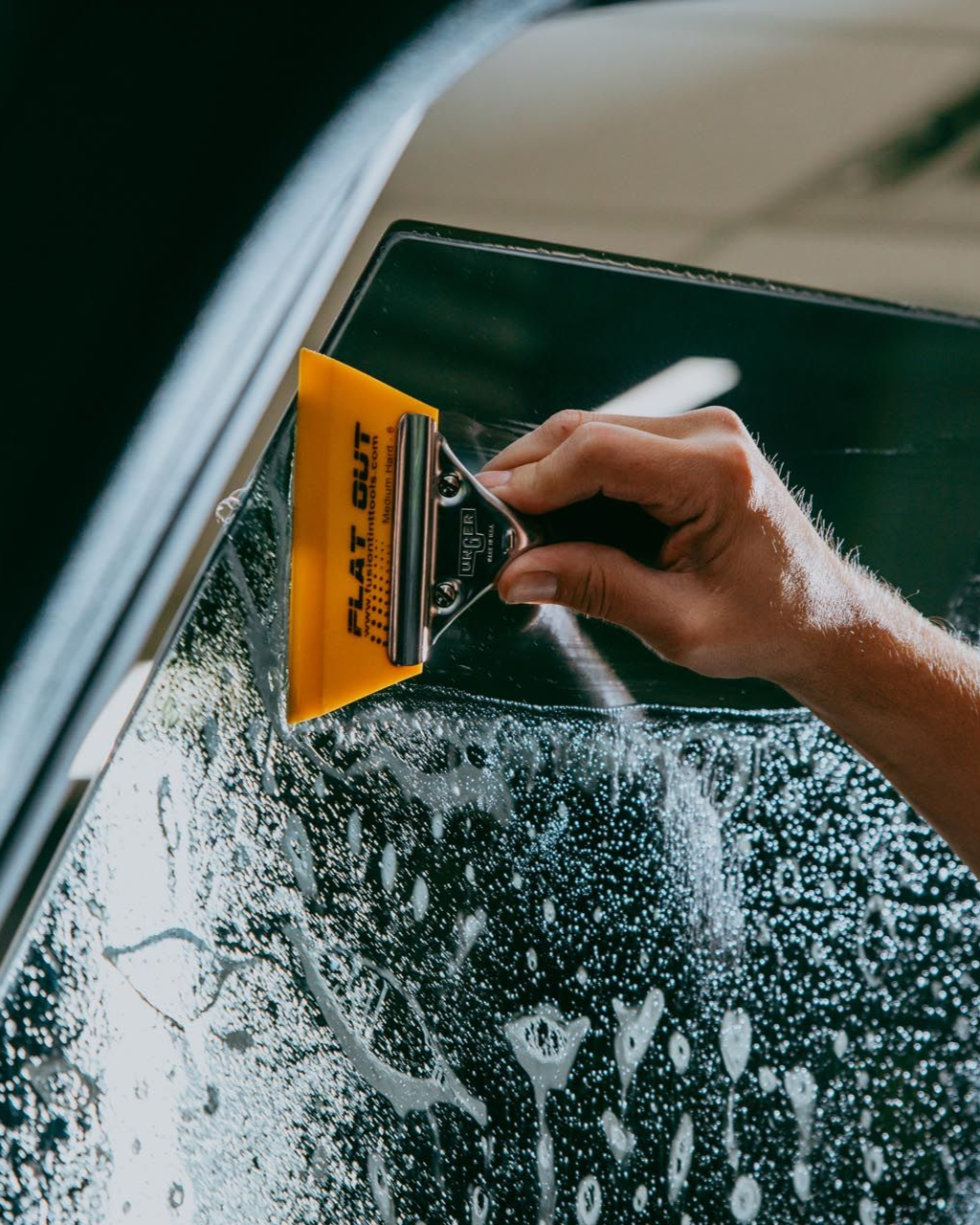 Person using a yellow squeegee to apply window tinting to a car window.
