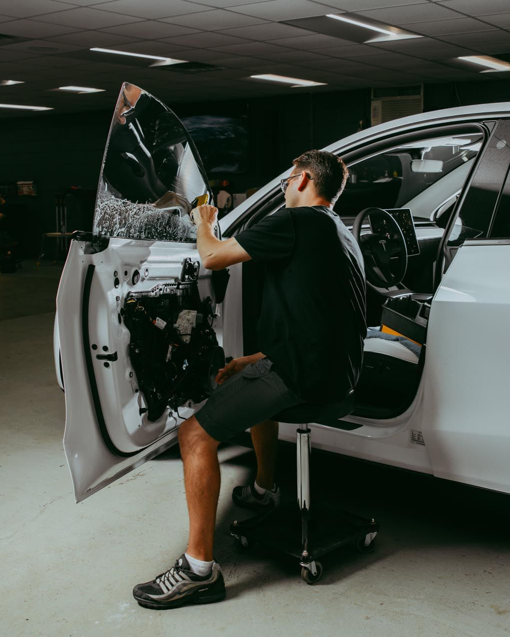 Man installing window tint on a car door, working in a garage.