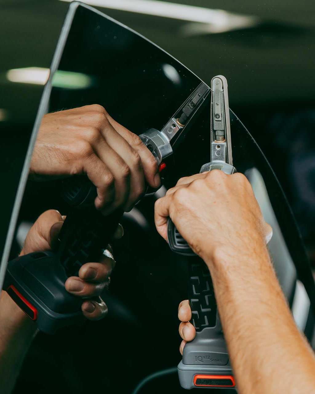Hands using two tools to work on tinted car window.