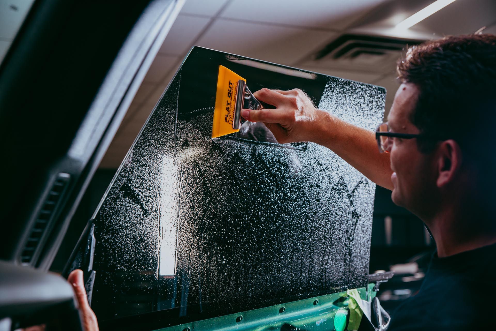 Person applying window tint to a car window with a squeegee.