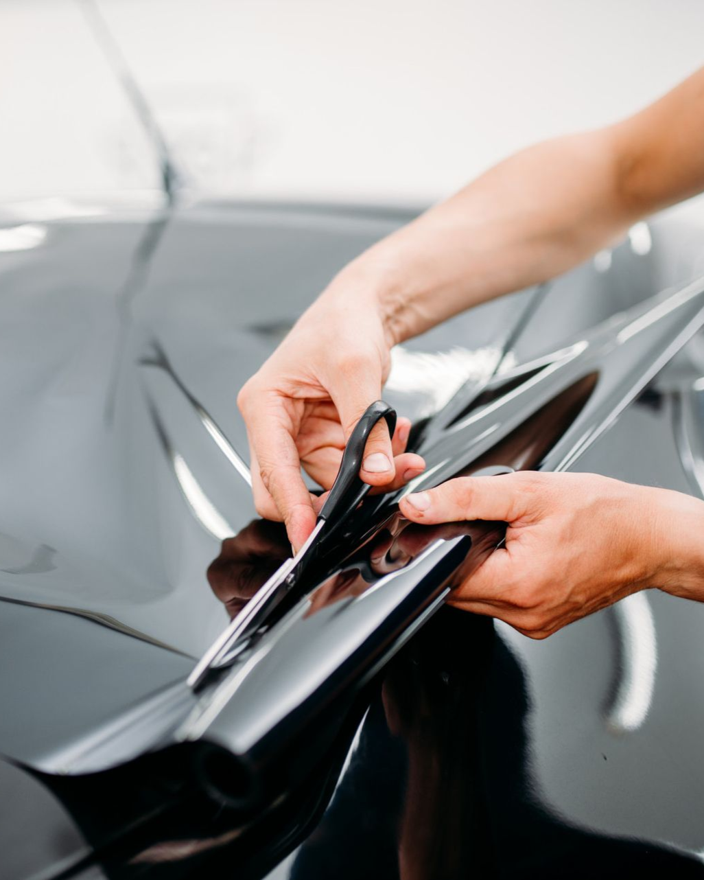 Hands trimming film on a black car door handle, indoors.