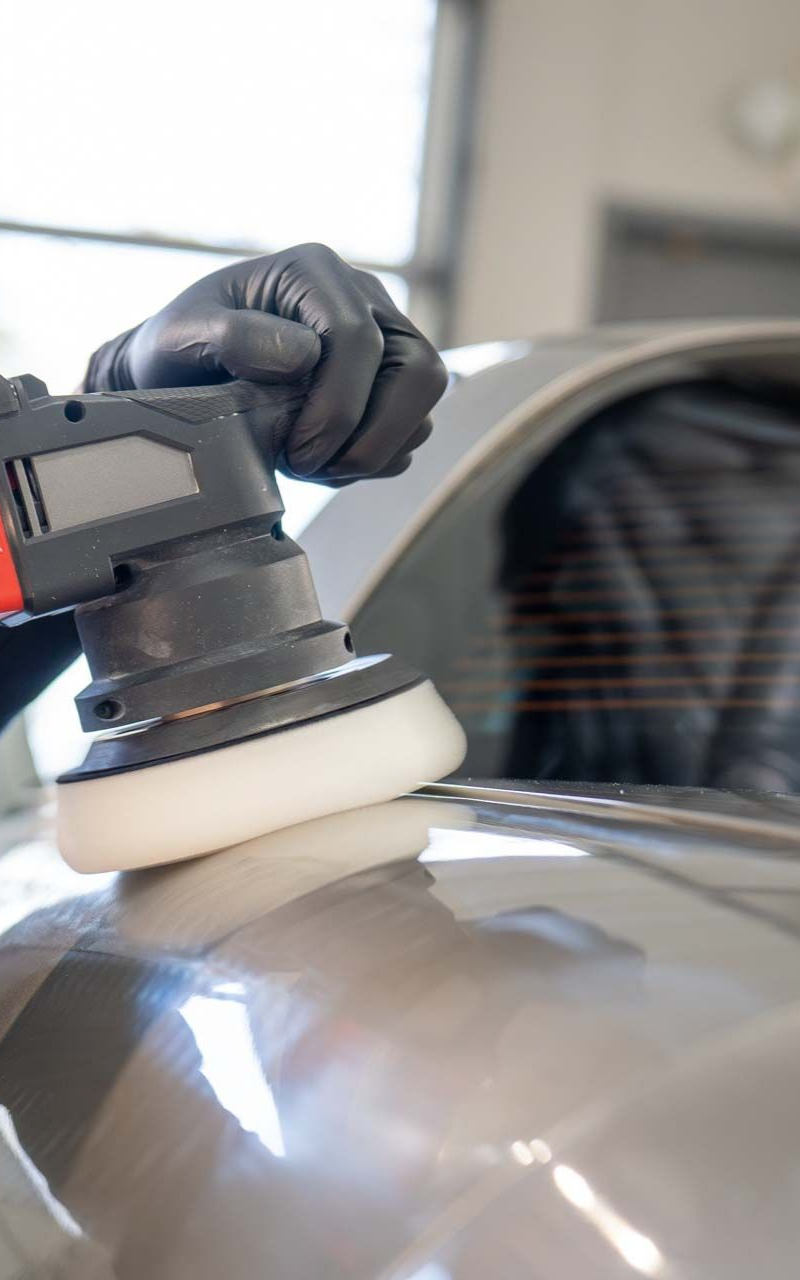 Person in black gloves using a polishing machine on a silver car.