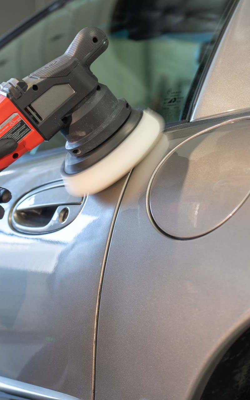 A person using a power buffer on a silver car to polish the surface.