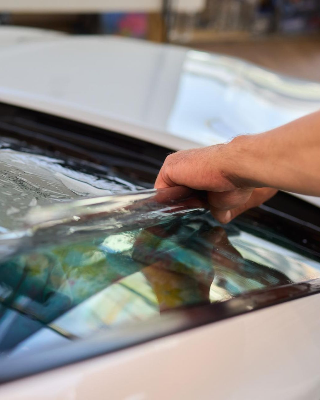 Hand peeling tinted film from a car window, close-up view.