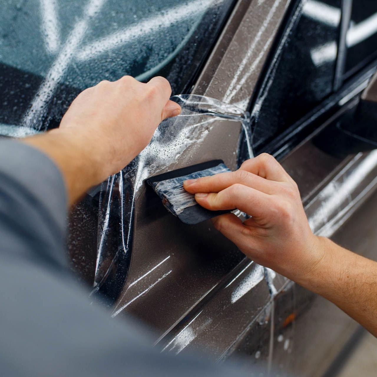 Person applying film to a car; using a squeegee.