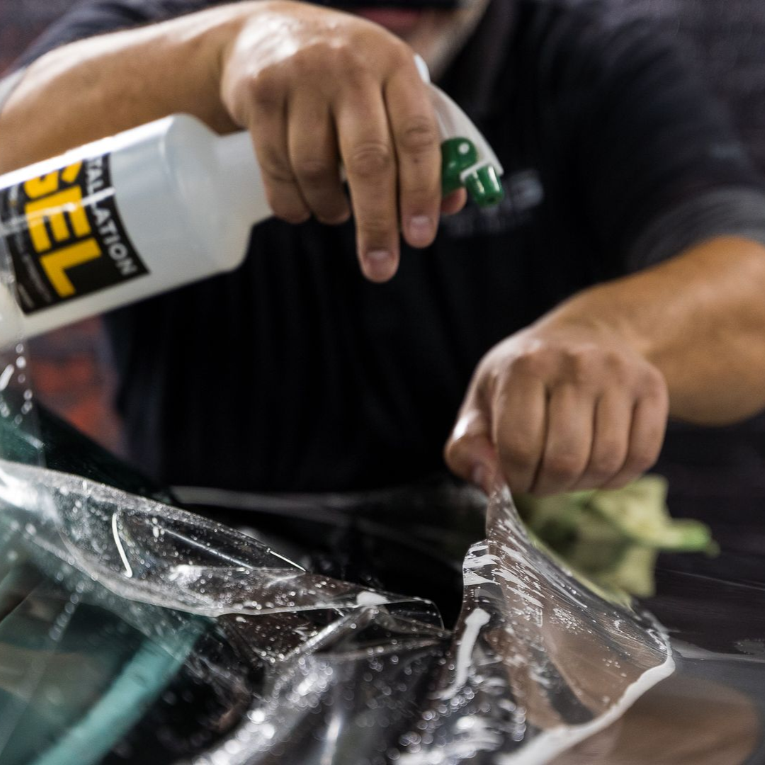 Person spraying liquid onto film over a windshield.