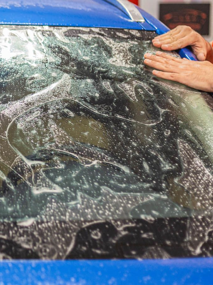 Person applying tint to a car window with a tool, indoors.