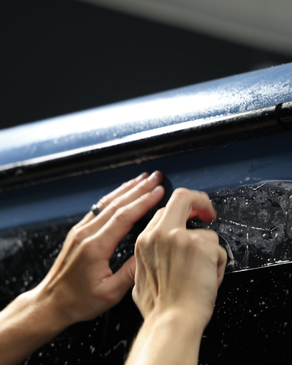 Hands peeling film from a dark blue car, close-up.
