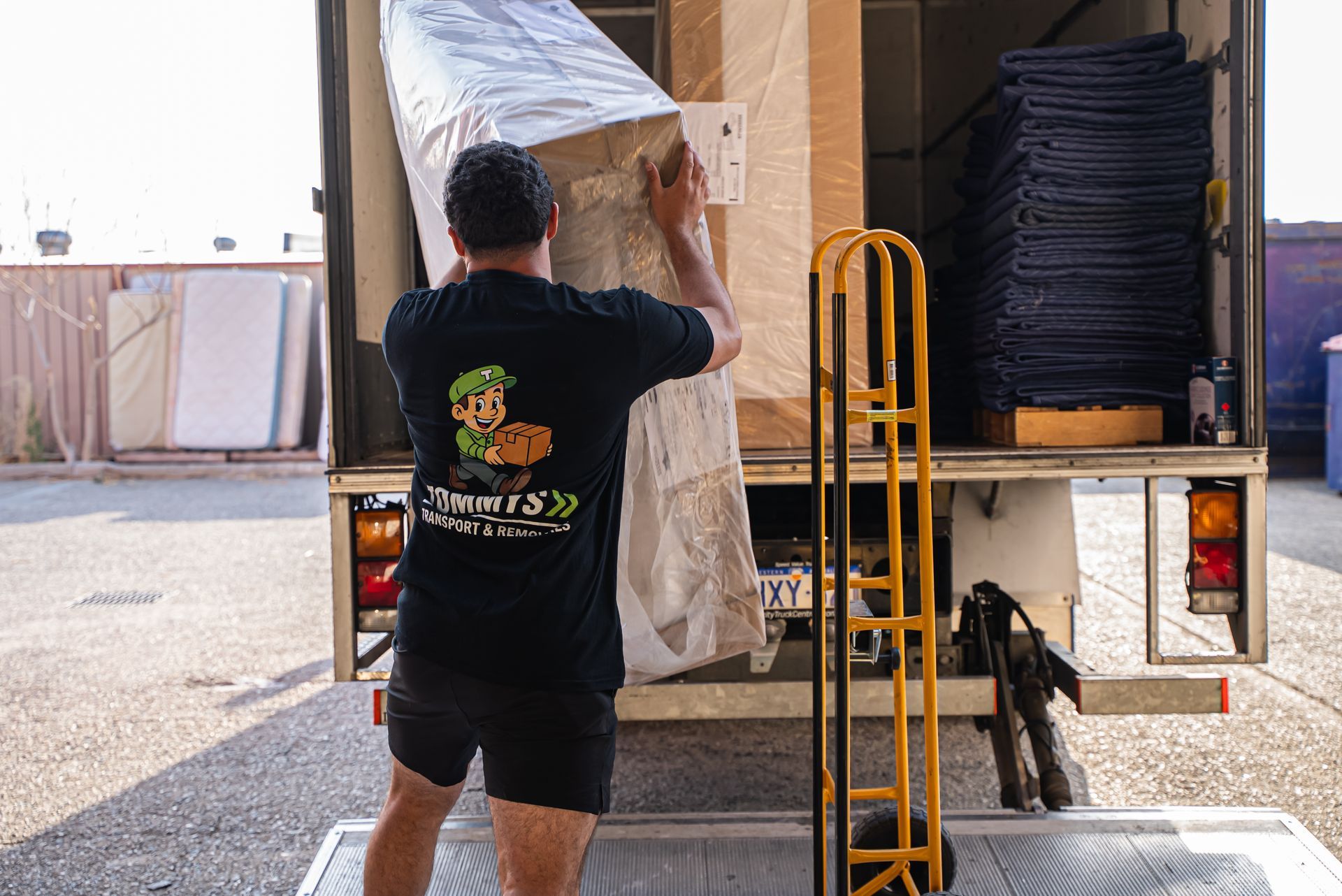Worker unloading a wrapped mattress from a removalist truck at a loading dock.
