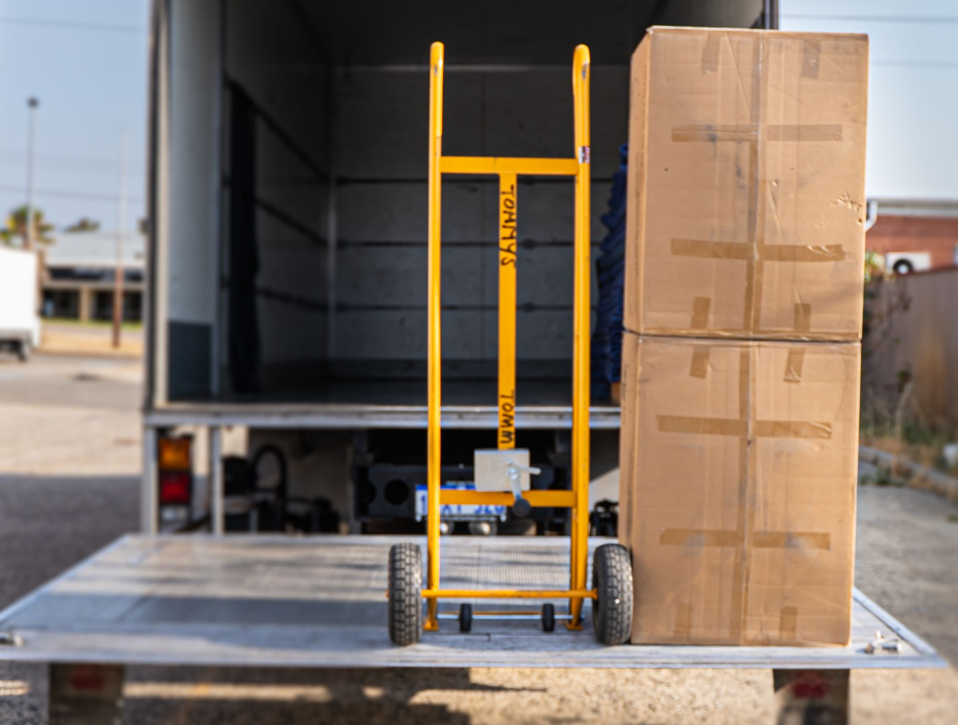 Yellow hand truck beside stacked cardboard boxes on a loading dock of a moving truck.