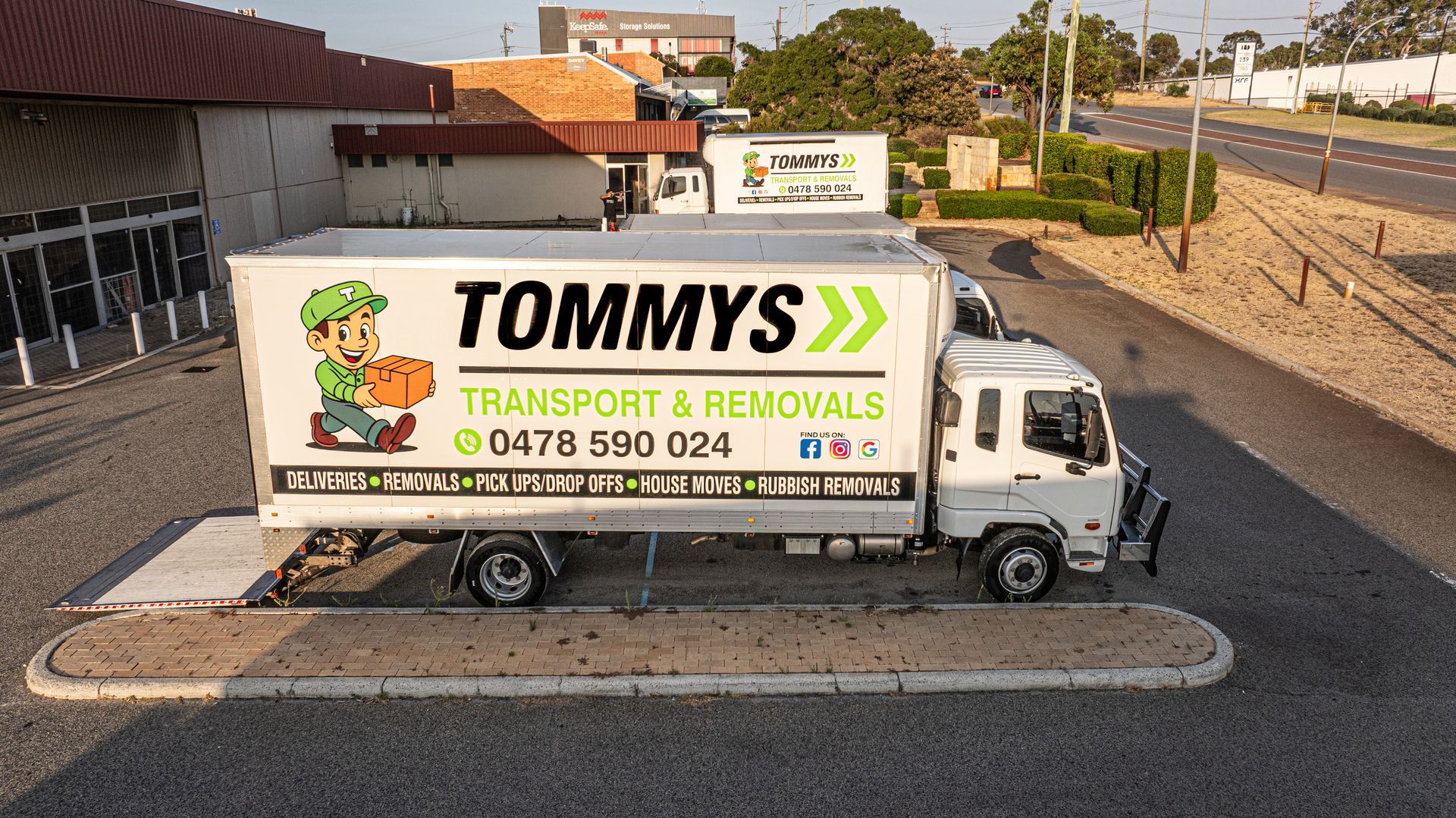 A white Tommys Transport & Removals truck parked in a gravel lot with a cartoon mascot on the side.