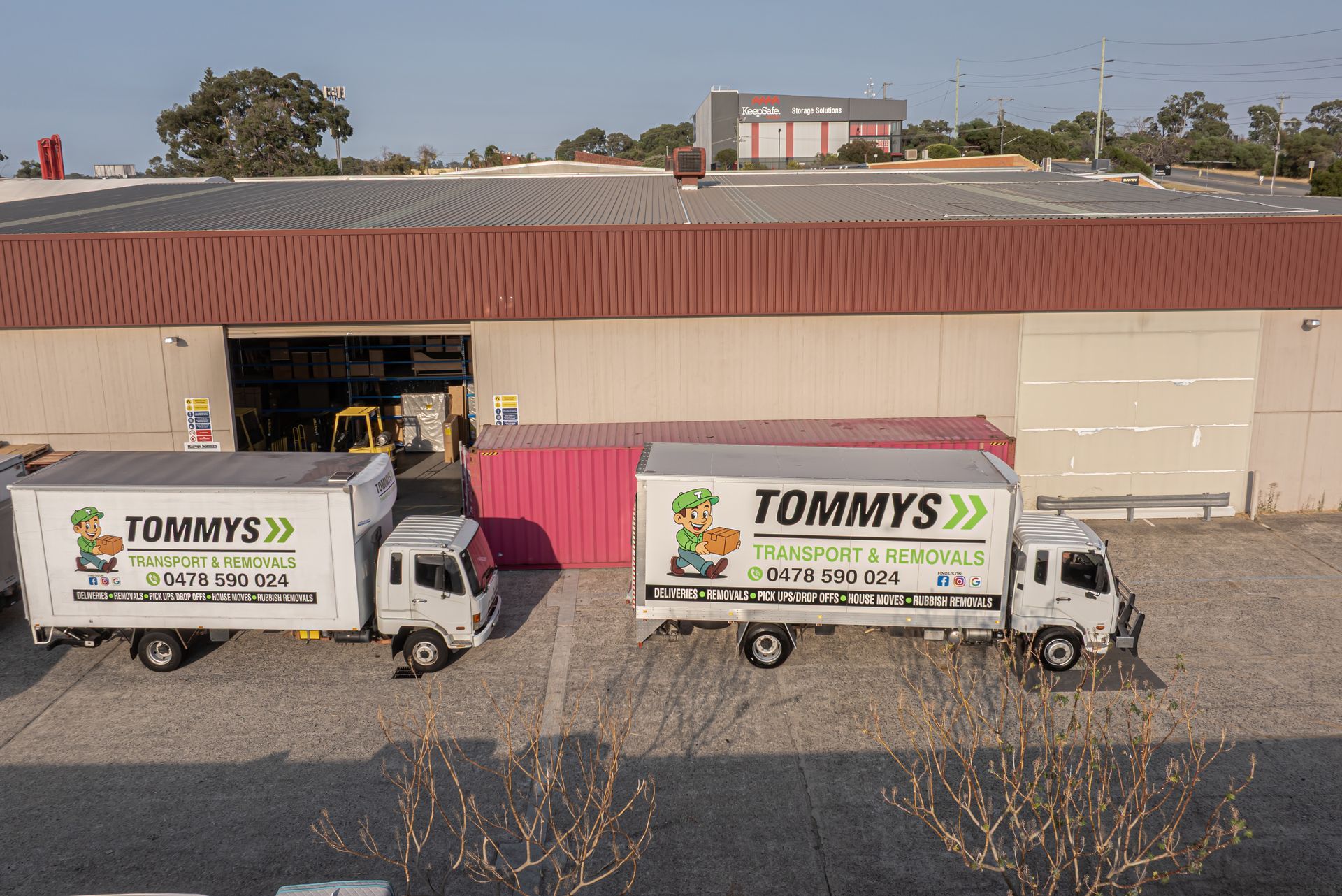 Two Tommy's Transport & Removals trucks parked outside a warehouse.