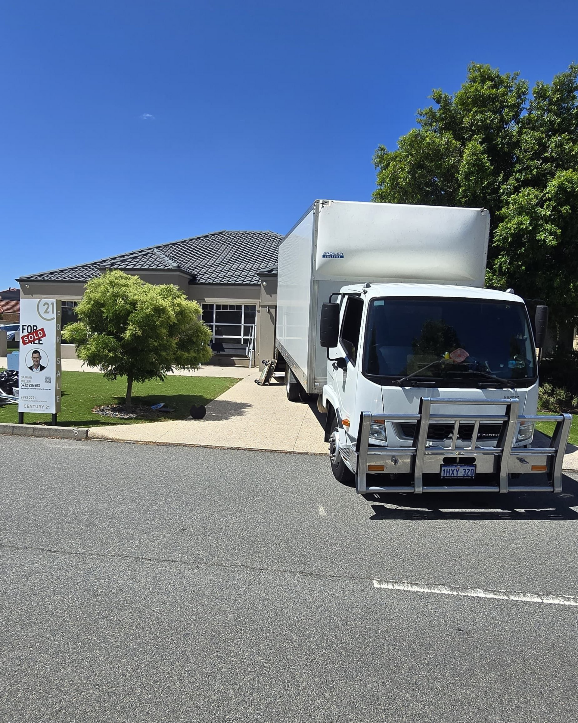 White moving truck parked in front of a building with gravel parking, sunny day.