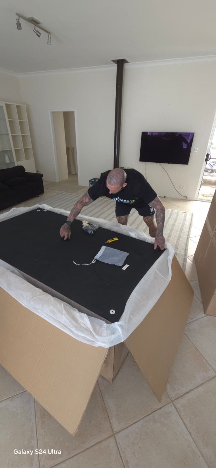 Joel the owner of Tommys transport and removals unpacking large furniture item for customer in Perth