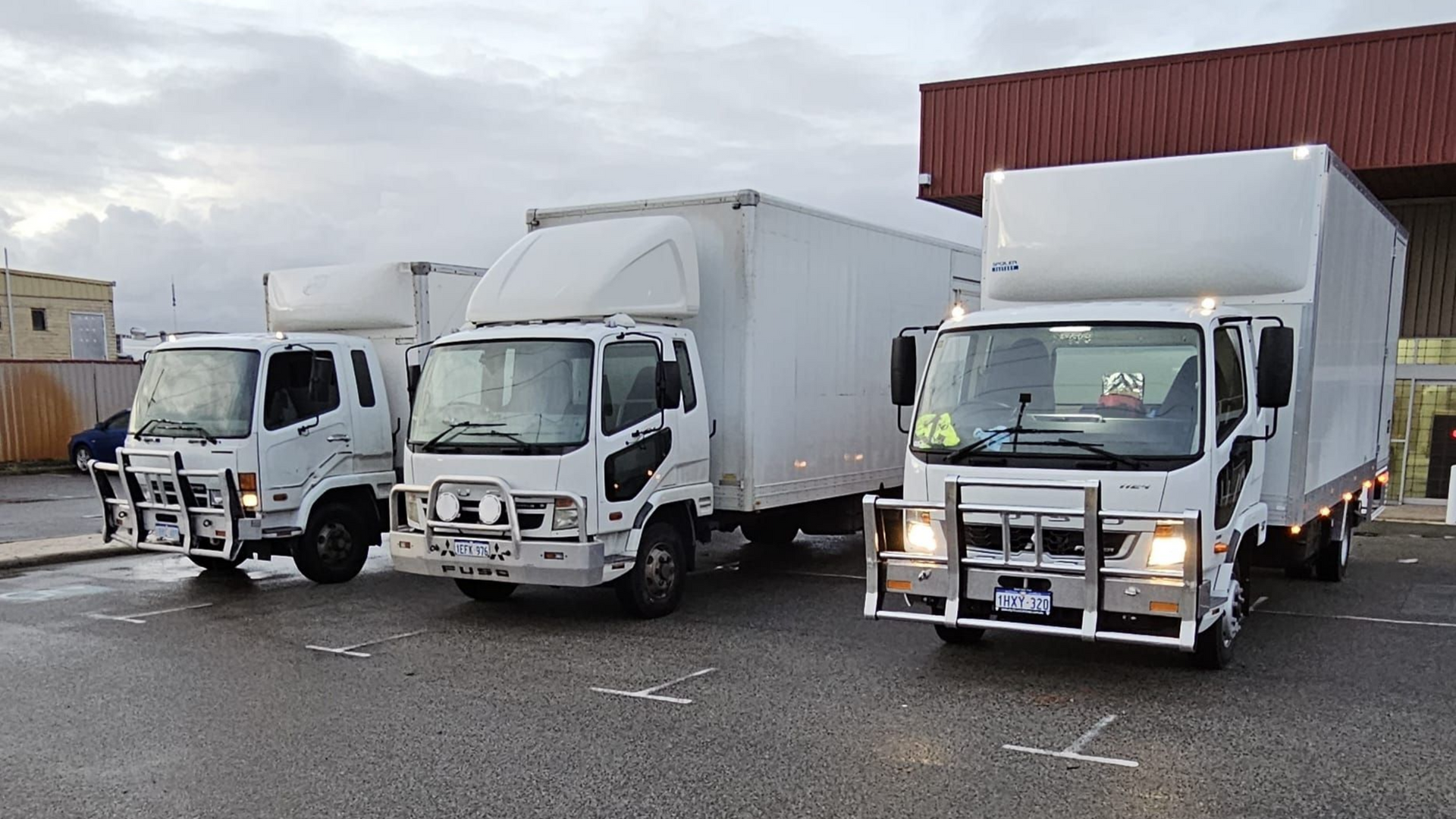 Three white box trucks parked in an outdoor lot, ready for loading/unloading.