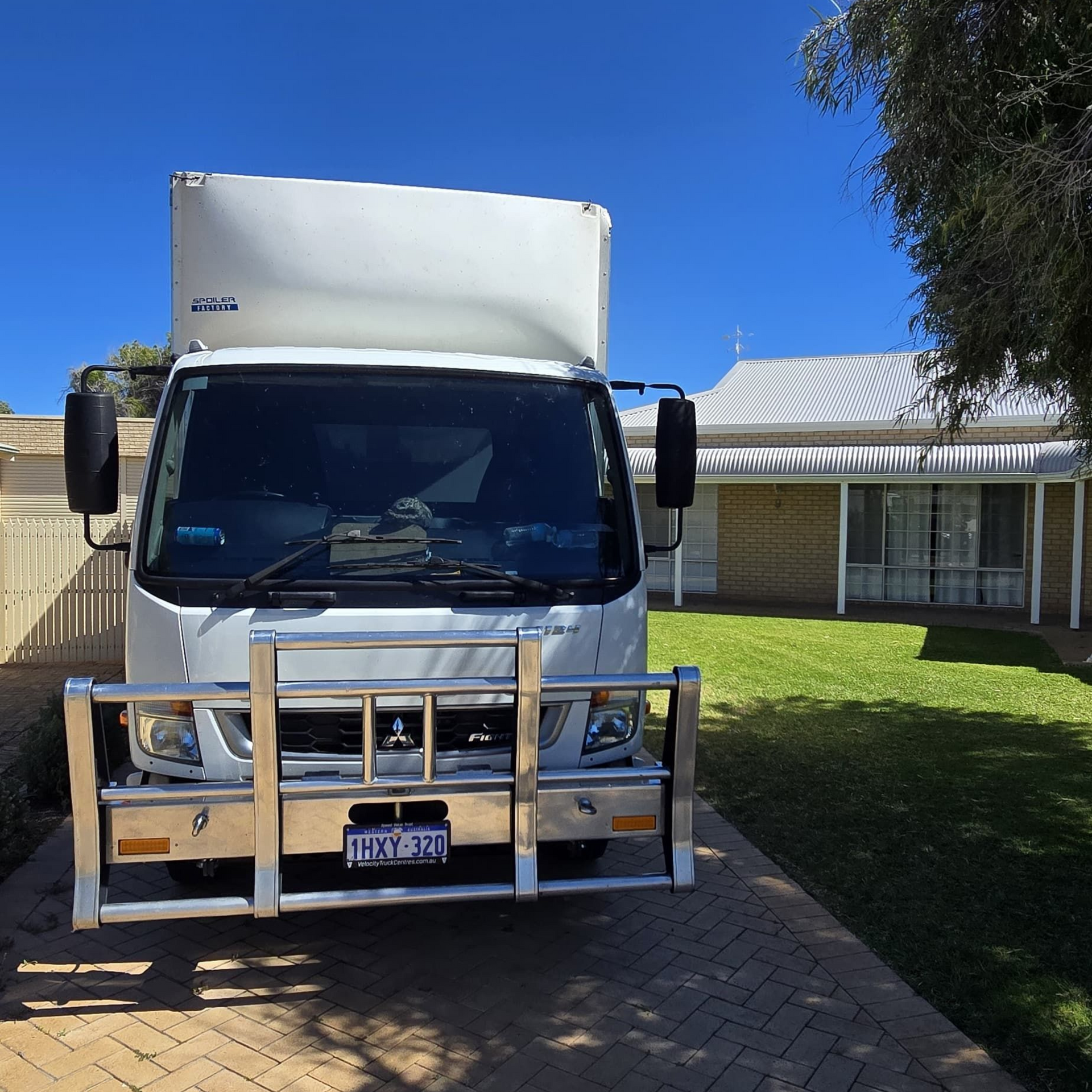 Tommy's Transport & Removals white moving truck parked in a driveway in front of a house on a sunny day.