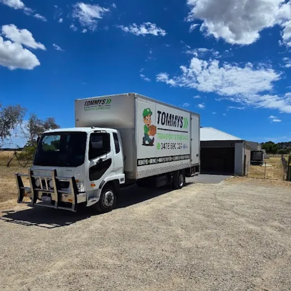 White moving truck parked on gravel driveway in front of a house on a sunny day.