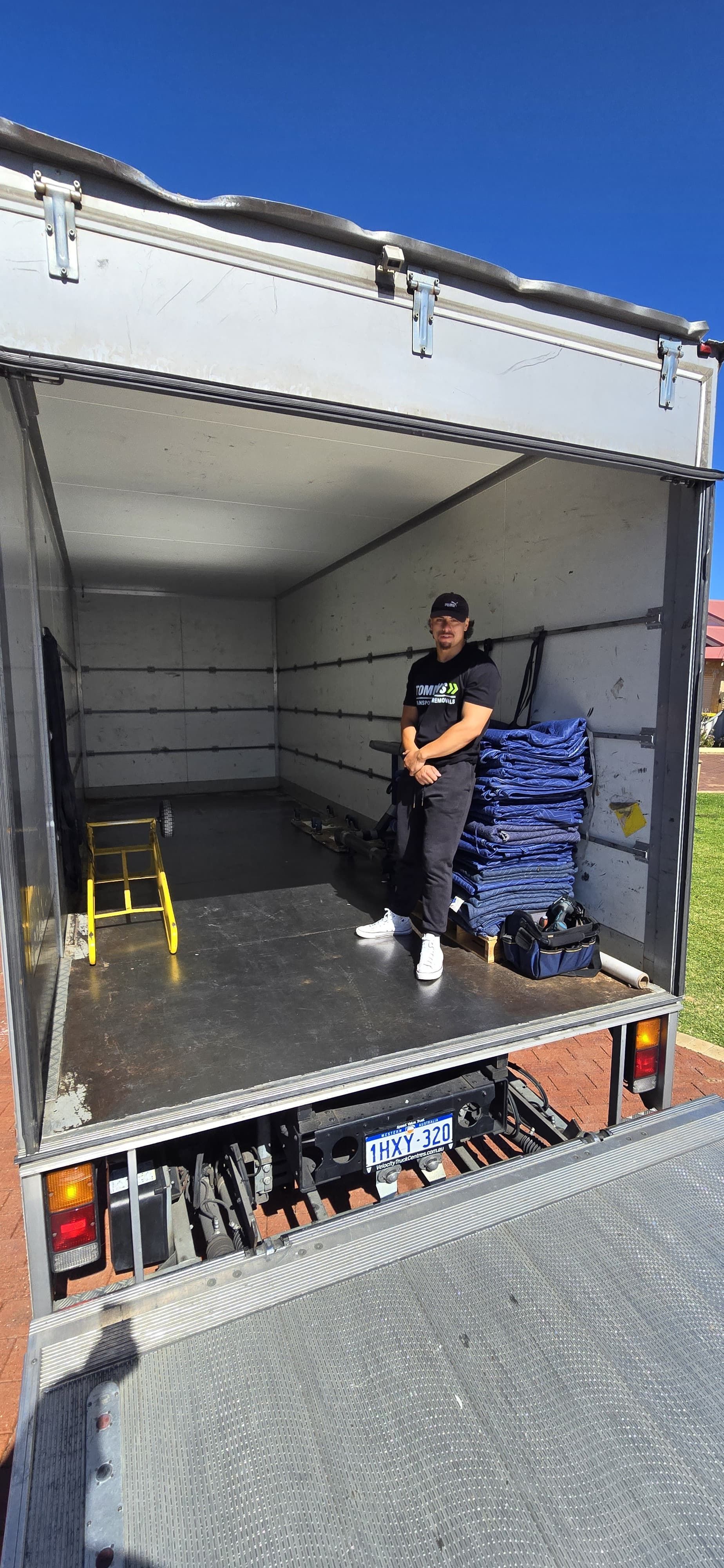 Man standing in an empty moving truck. Blue sky. Loading ramp is down.