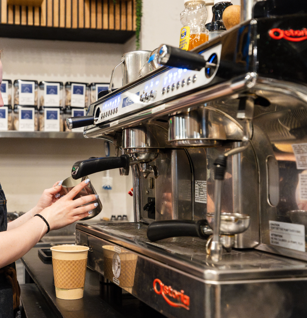 A woman is pouring coffee into a cup at a coffee shop