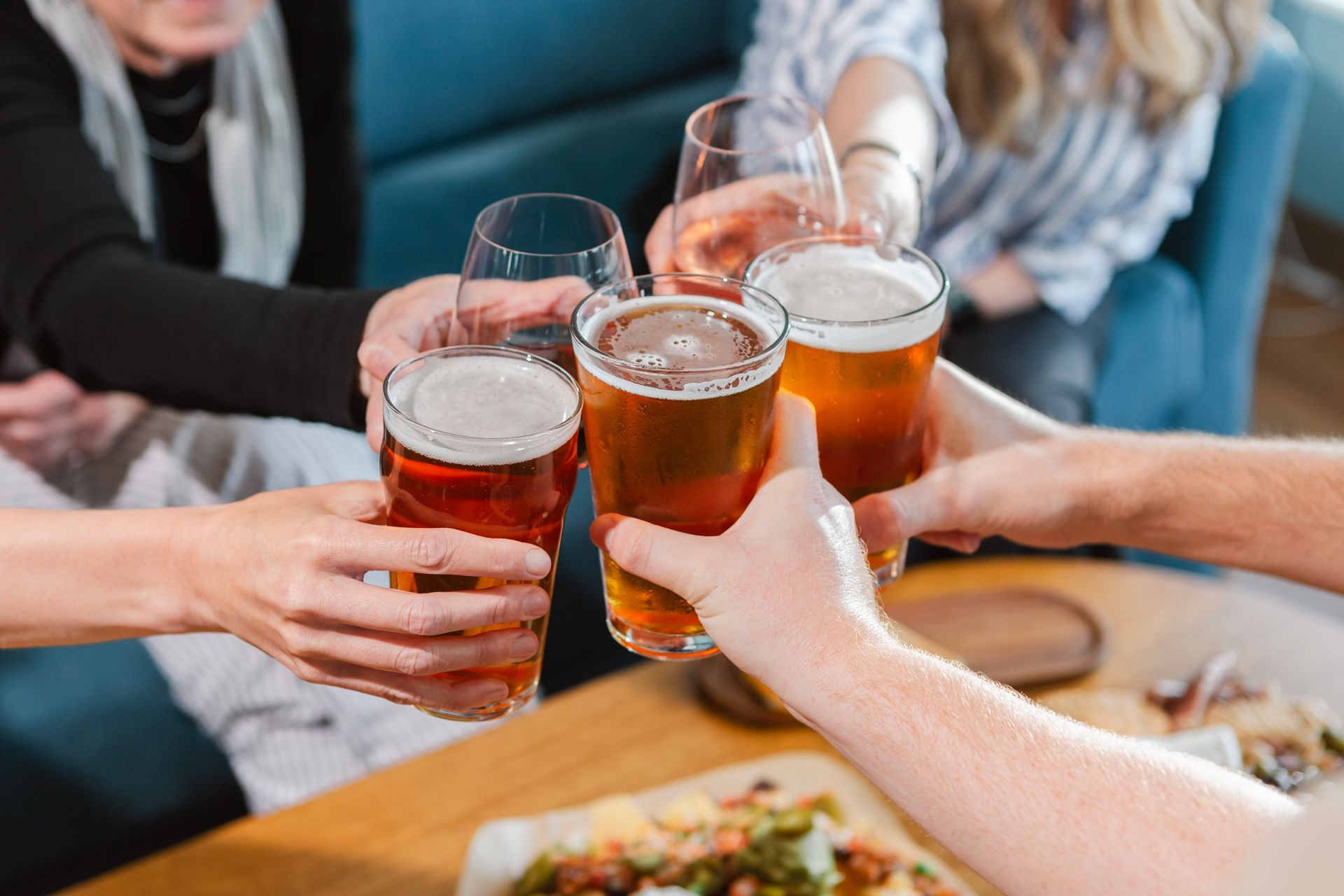 Hands toasting beer and wine glasses at a table with food.