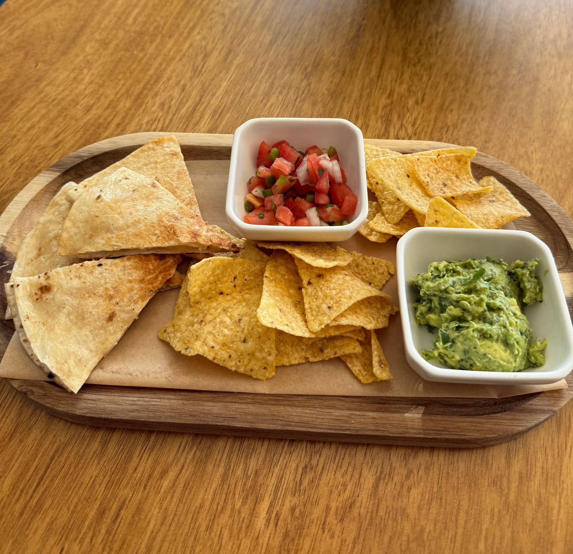 Wooden platter with chips, guacamole, salsa and quesadilla.