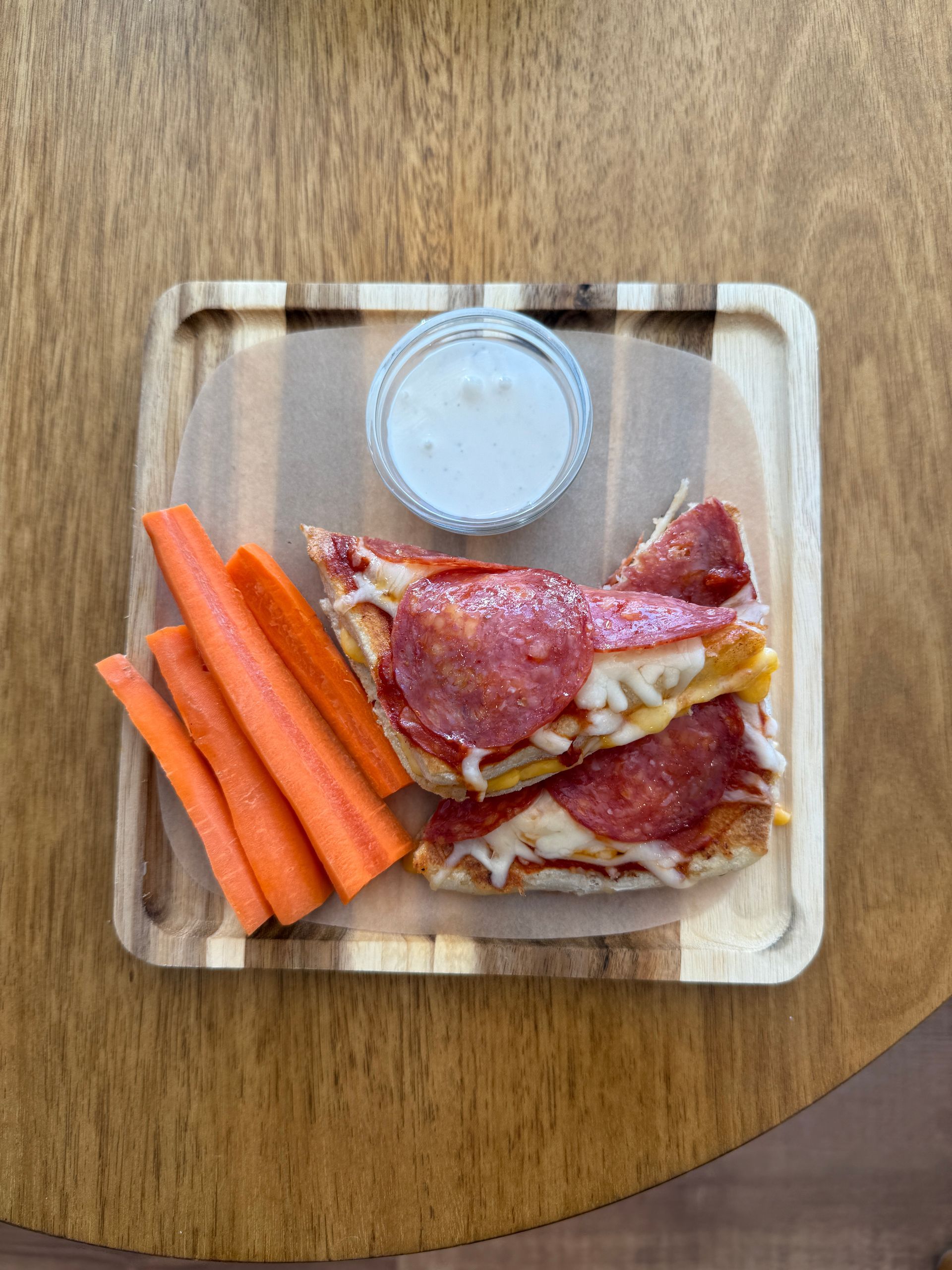 Pizza grilled cheese sandwich with carrot sticks and ranch on a wooden tray.