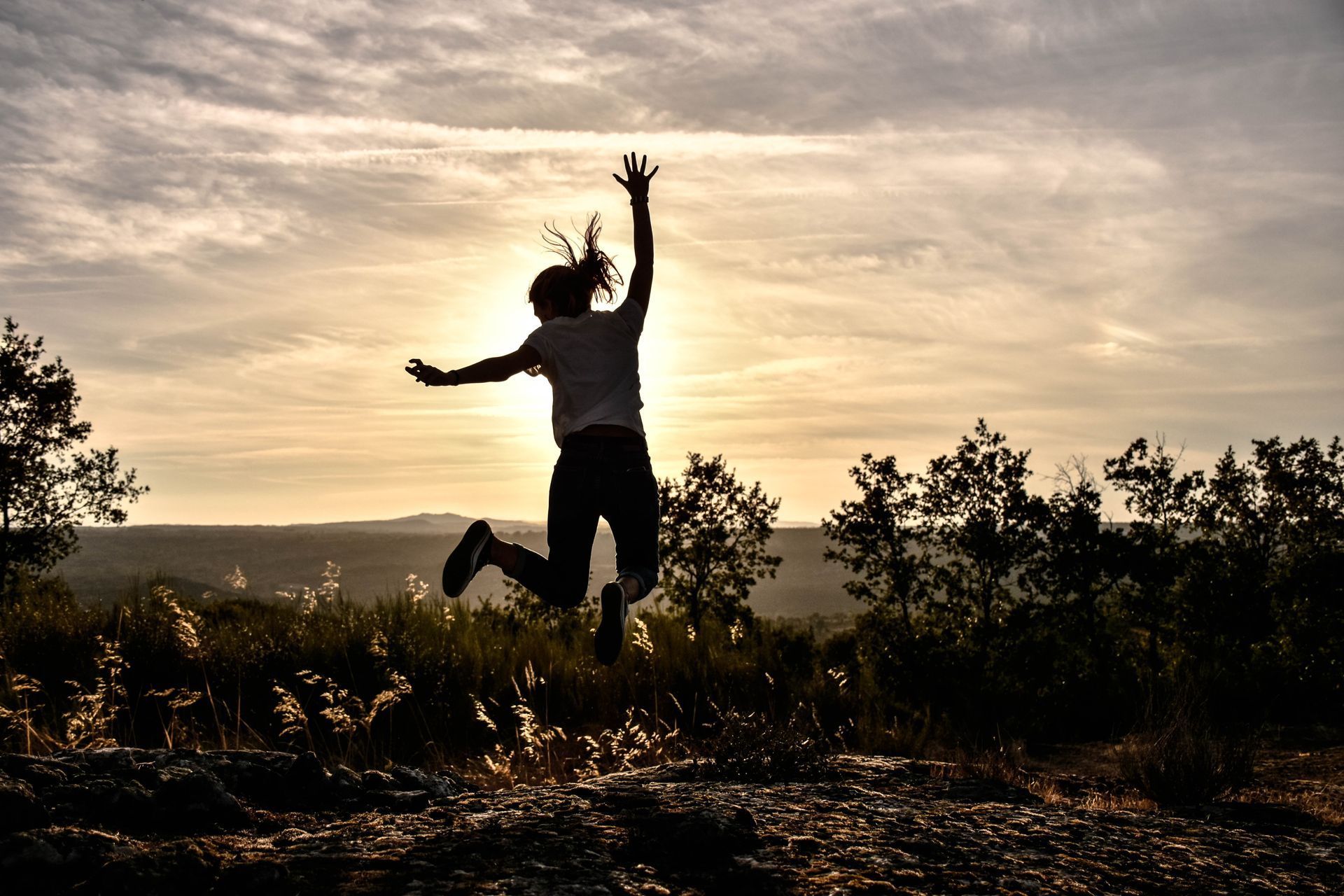 Silhouette of person jumping with arms raised against a sunset.